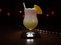 Cocktail Miami Vice avec une moitié blanche crémeuse et une moitié rouge fruitée, garni d'un quartier d'ananas et d'un petit parasol rose.