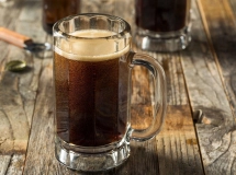 Un grand verre à cocktail avec du soda brun foncé, une mousse crémeuse débordante sur le dessus, décoré d'une paille rayée verte et blanche, marqué du logo "BEST DAMN" à l'avant.