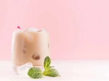 Verre à cocktail rempli de Midnight Mint crémeux avec une feuille de menthe verte décorative sur le dessus, posé sur une nappe beige avec des baies rouges en arrière-plan.
