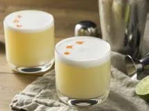 Verre à cocktail rempli de pisco sour, avec une mousse blanche onctueuse et quelques gouttes de bitters décorant le dessus.