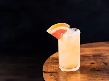 Un verre allongé rempli d'un cocktail rosé pâle avec de la glace pilée, garni d'une tranche de pamplemousse.
