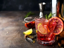 Verre de cocktail rempli de Greyhound rose pâle, garni d'un brin de romarin, avec un demi-pamplemousse flou en arrière-plan.