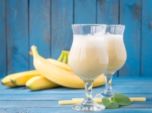 Deux verres remplis de banana daiquiri glacé, garnis de tranches de banane et de citron vert, avec une feuille de menthe sur le dessus, posés sur un dessous de verre à motifs bleus et blancs.