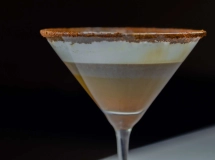 Un verre à cocktail rempli d'une boisson crémeuse de couleur beige, surmontée d'une légère pincée de cannelle en poudre.