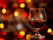 Verre à cognac rempli de cocktail ambré brillant sur fond de lumières floues rouges et oranges.