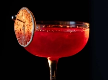 Verre à cocktail rempli d'un liquide rouge foncé surmonté d'un zeste d'orange.