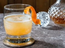 Verre à whisky avec un cocktail ambré, garni d'un zeste de citron.
