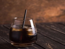 Verre de cocktail rempli de boisson sombre avec glaçons, accompagné de deux pailles rouges.