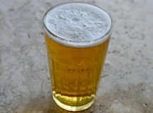 Verre à bière rempli d'un cocktail Radler jaune pâle avec une mousse crémeuse sur le dessus, posé sur une surface en pierre grise.