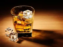 Un verre de whisky ambré rempli de glaçons, posé sur une table en bois éclairée par une lumière chaude.