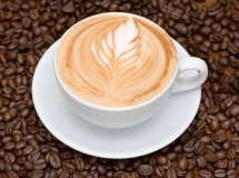 Une tasse de café chaud avec de la mousse crémeuse sur le dessus, entourée de grains de café éparpillés sur un fond de tissu en toile de jute.