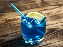 Un verre à cocktail rempli de liquide bleu vif, garni de glaçons et d'une tranche de citron sur le bord.
