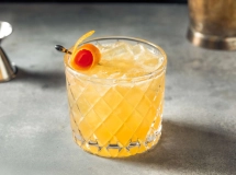 Verre de cocktail Amaretto Sour garni de cerises, posé sur un sous-verre.