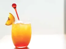 Verre de cocktail avec dégradé de couleurs rouge en bas et jaune en haut, garni d'une tranche d'orange et d'une cerise rouge.