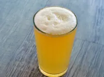 Verre à pied rempli d'un cocktail mousseux jaune pâle sur une table en bois, éclairé par la lumière.