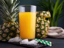 Deux verres de smoothie jaune vif à l'ananas, garnis d'un morceau d'ananas frais, posés sur une table en bois.