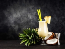 Cocktail piña colada crémeux dans un verre ouragan, garni d'une tranche d'ananas, d'une cerise et d'un petit parasol rose.