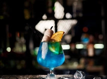 Verre à cocktail avec une boisson en dégradé de bleu au violet, garni de glaçons et une paille noire.
