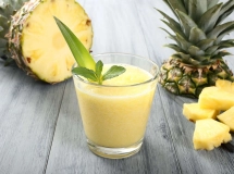 Deux verres de smoothie d'ananas, avec un morceau d'ananas frais décorant le bord du verre, sur une table en bois.
