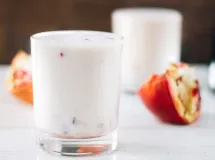 Trois verres de lassi, une boisson indienne crémeuse et mousseuse garnie de morceaux de pistache, sur une nappe foncée.