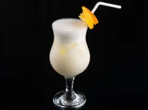 Un verre de margarita blanche garni de noix de coco râpée, avec une tranche d'orange et une cerise rouge en décoration sur le bord du verre.