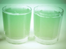 Un verre à shot transparent rempli d'un cocktail vert vif éclairé par une lumière douce.