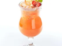 Un cocktail rose pâle servi dans un verre rempli de glaçons, garni d'une tranche d'ananas et d'une cerise, avec une paille bleue.