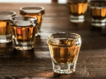 Trois verres à shot remplis d'une boisson ambrée, posés sur une table en bois sombre.