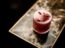 Verre de cocktail Pink Lady avec une garniture de fraise fraîche, rondelle d'ananas et spirale de zeste de citron.