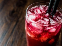 Six verres de cocktail Alabama Slammer disposés en rangée, avec un dégradé de couleurs vives allant du rouge au jaune, garnis de tranches d'orange et de pailles noires.