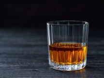 Un verre de cocktail carré rempli d'un liquide ambré posé sur une surface en bois.