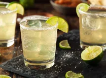 Un verre à cocktail rempli d'une margarita jaune pâle avec un bord glacé au sel et garni d'une tranche de citron vert.