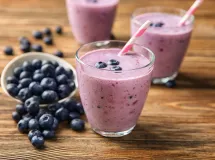 Verre de smoothie rose crémeux avec des myrtilles fraîches sur une brochette décorative, posé sur une nappe bleue.