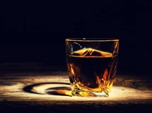 Un verre à whisky rempli de glaçons et de whisky ambré posé sur une surface en bois sombre.