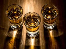 Trois verres à shot remplis d'un cocktail ambré, avec des gouttes de condensation sur les verres.