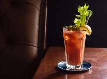 Cocktail Bloody Maria dans un verre à whisky garni d'une tige de céleri, avec une bouteille en arrière-plan.