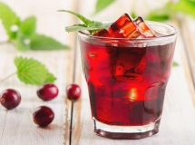 Un verre de cocktail « bleeding surgeon » avec des couches de couleurs rose vif et blanc, garni de glaçons translucides et un bâton à mélanger noir, tenu par une main.