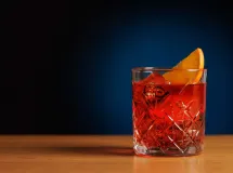 Un verre de Negroni sur fond noir, garni d'un zeste d'orange et contenant un gros glaçon.