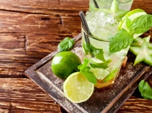 Verre de Mojito alsacien avec de la menthe fraîche, tranches de citron vert, et glaçons, posé sur une table en bois, avec une demi-lime à côté.