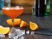 Verre à cocktail rempli d'un liquide ambré, garni d'une tranche d'orange.