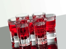 Trois verres à shot remplis d'un liquide rouge vif, disposés sur une surface noire brillante.