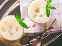 Verre de lassi blanc crémeux garni d'une feuille de menthe, avec une paille rayée sur une surface en bois.