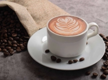 Tasse de café crémeux sur un tissu de jute, entourée de grains de café répartis autour.