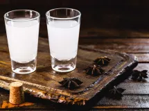 Verre à martini contenant un cocktail doré avec un zeste d'agrume, posé sur un comptoir en bois avec un arrière-plan flou de bouteilles et lumières tamisées.