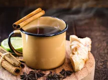 Tasse de masala chai servie chaude avec bâtons de réglisse noire en garniture, entourée d'épices entières comme la cardamome, le clou de girofle, la cannelle, l'anis étoilé et un quartier de citron.