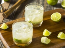 Un verre de Caipiroska avec des quartiers de citron vert, des glaçons et une paille transparente sur fond noir.