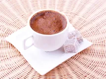 Tasse de chocolat chaud crémeux posé sur une soucoupe blanche.