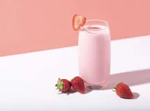Un verre à cocktail contenant un smoothie crémeux, garni d'une fraise rouge et avec deux pailles colorées.