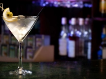 Un verre à martini transparent rempli d'un cocktail clair, garni d'une olive verte et accompagné d'un agitateur métallique.