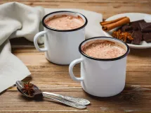 Une tasse de chocolat chaud crémeux servie dans une tasse blanche sur une soucoupe, avec des bulles à la surface de la boisson.